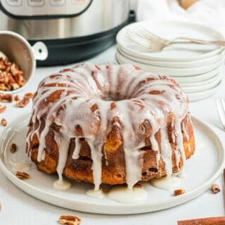 Loaf of cinnamon roll bread on a white serving plate and drizzled with icing.