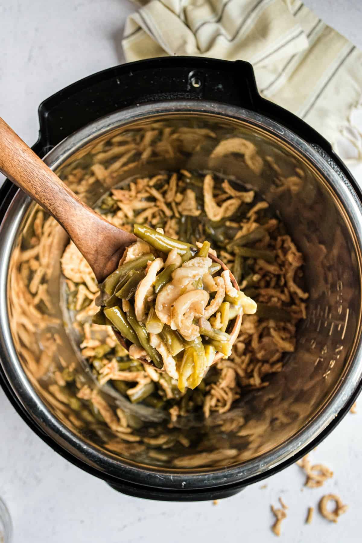 Instant pot green bean casserole being lifted by wooden spoon.