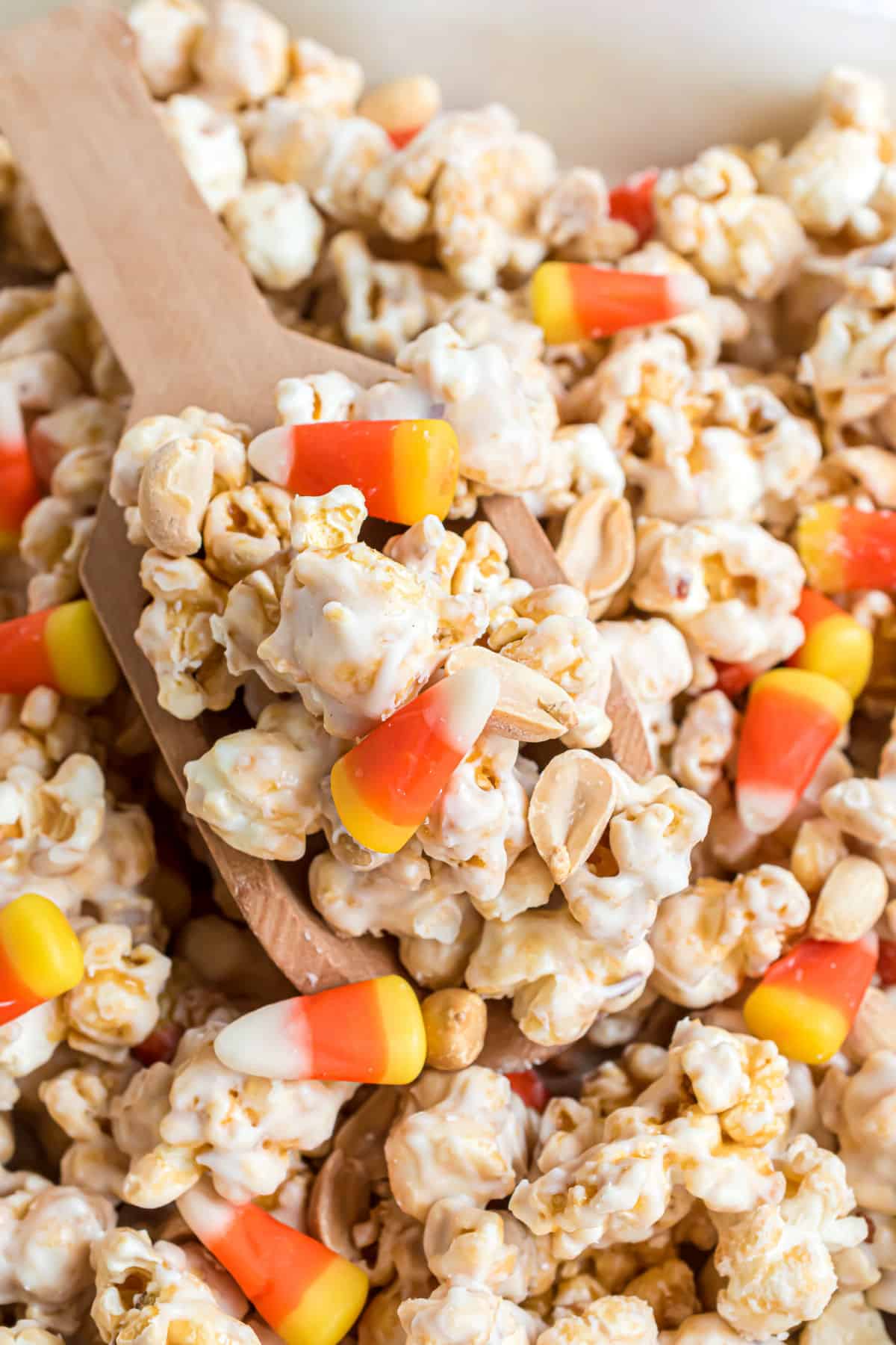 Caramel corn with candy corn being served with wooden spoon.