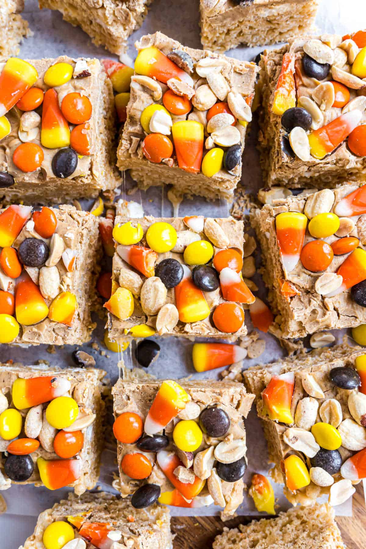Top view of peanut butter candy corn krispie treats, topped with peanuts and colorful chocolate candies.