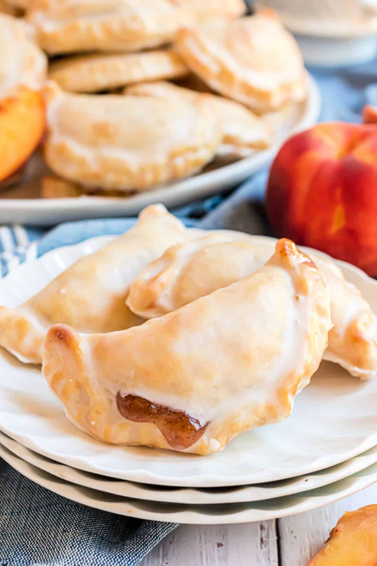 Peach hand pies served on a stack of white ruffled plates.