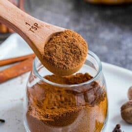 Small glass jar with homemade pumpkin pie spice substitute being scooped with a teaspoon.