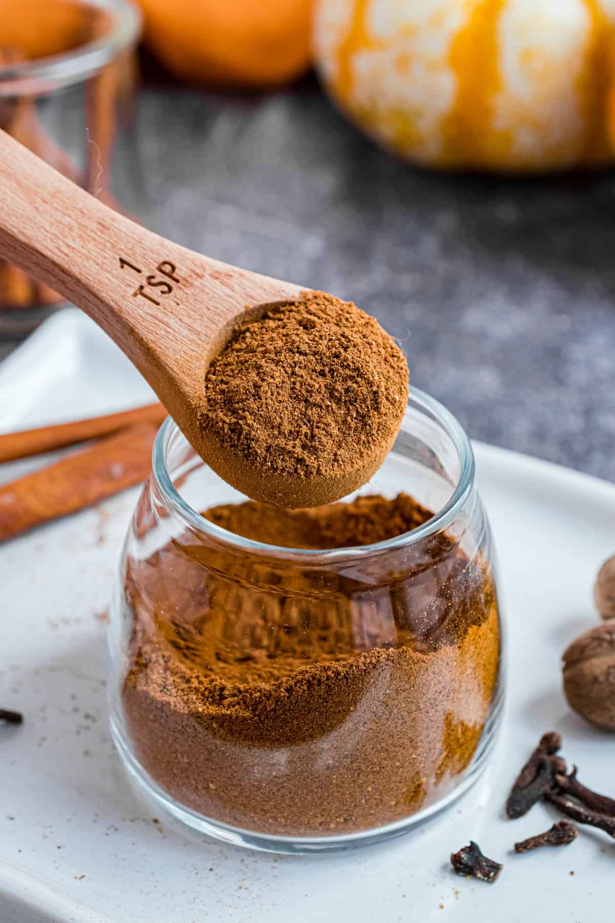 Small glass jar with homemade pumpkin pie spice substitute being scooped with a teaspoon.