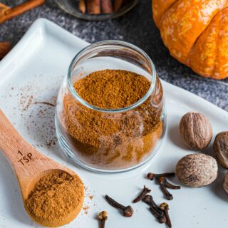 Pumpkin pie spice blend in a clear glass jar with a wooden teaspoon.