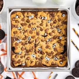 Spooky brookies: A brownie topped with cookie dough, chocolate chips, and candy eyes in a square baking pan.
