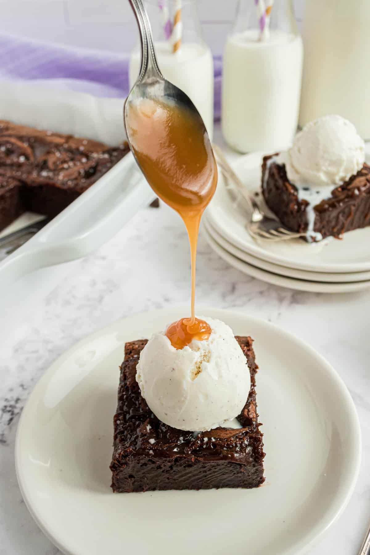 Brownie on a plate with caramel sauce being drizzled on ice cream.