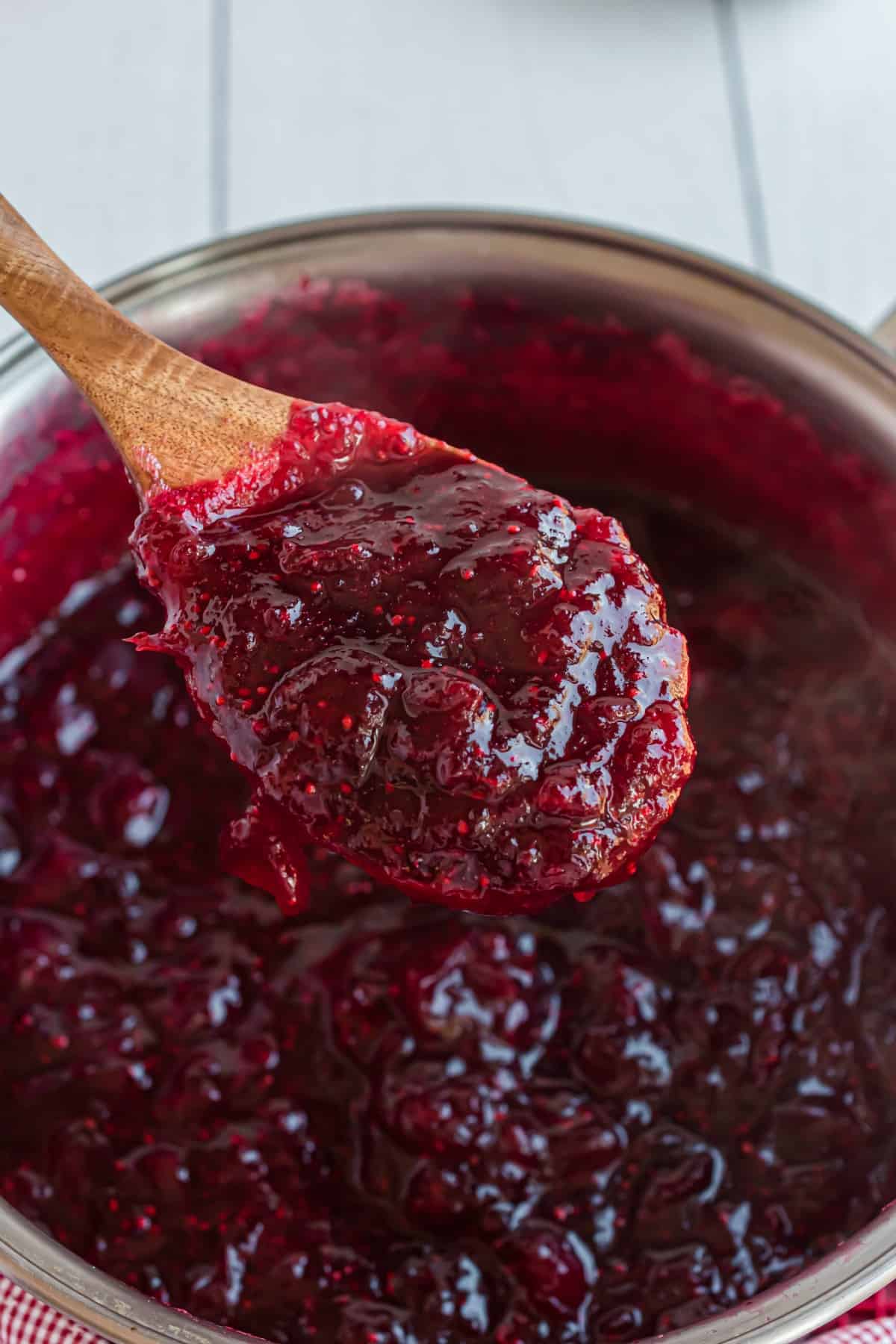 Homemade cranberry sauce in pot on a wooden spoon.