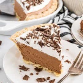 A slice of French silk pie topped with whipped cream and chocolate shavings sits on a white plate.