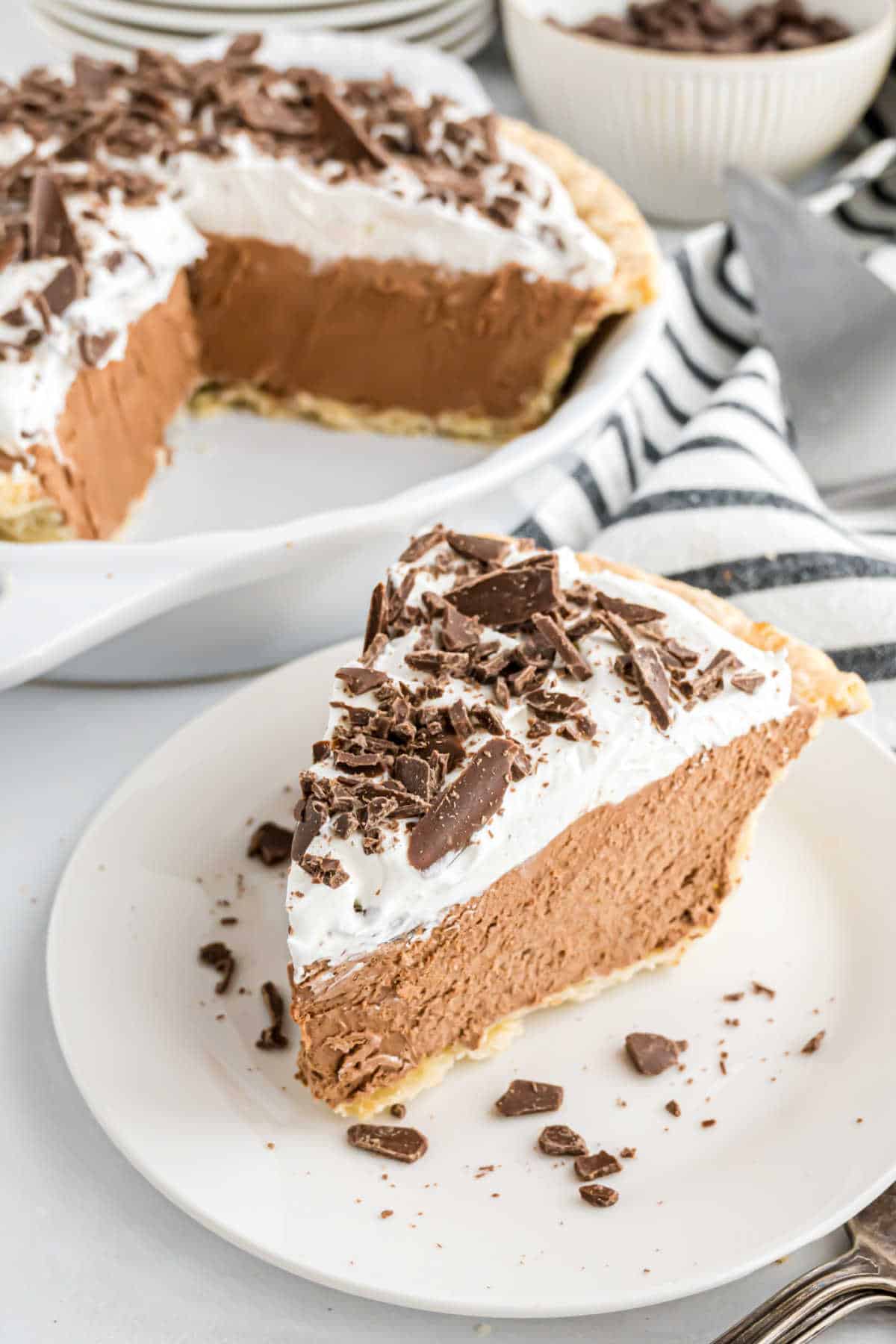A slice of decadent french silk pie with whipped topping and chocolate shavings on a white plate.