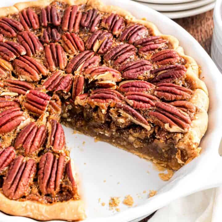 Pecan pie in white pie plate with a slice removed.