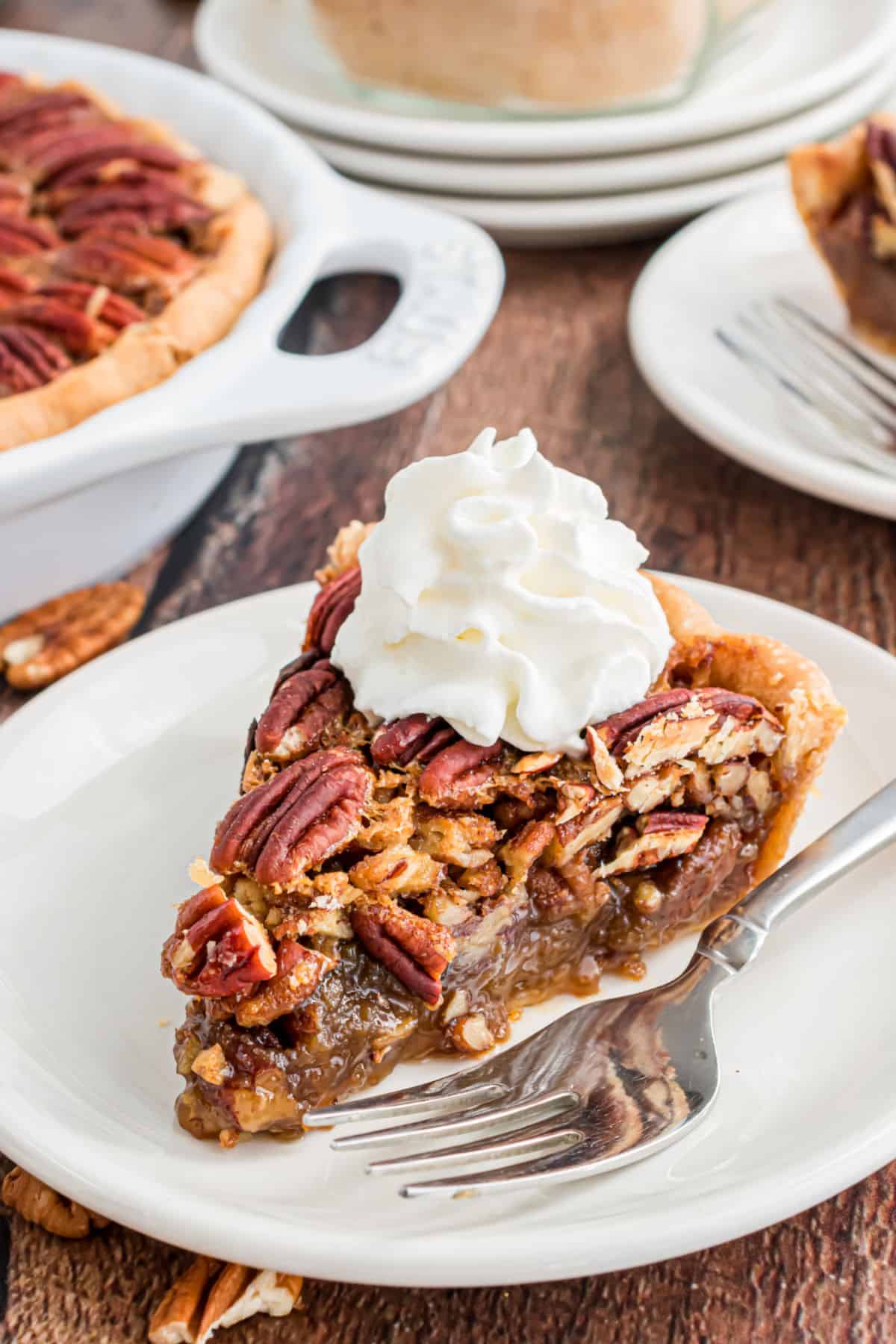 Slice of pecan pie on a white plate topped with whipped cream.