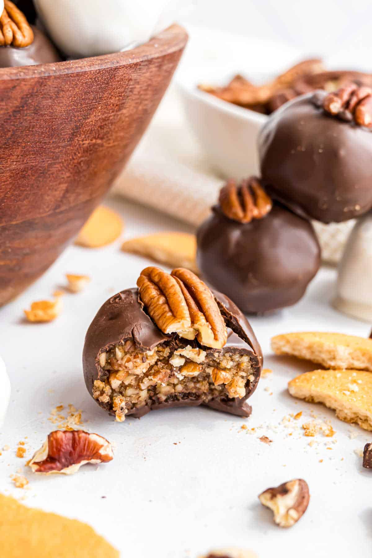 Chocolate-covered pecan pie truffle with a bite taken out, topped with pecans, and surrounded by cookie crumbs.