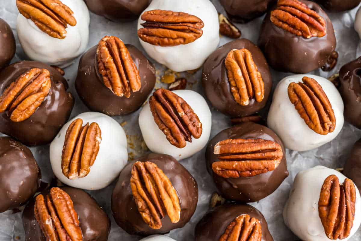 Close-up of pecan pie truffles, both chocolate and white-coated, topped with pecan halves and arranged closely together.