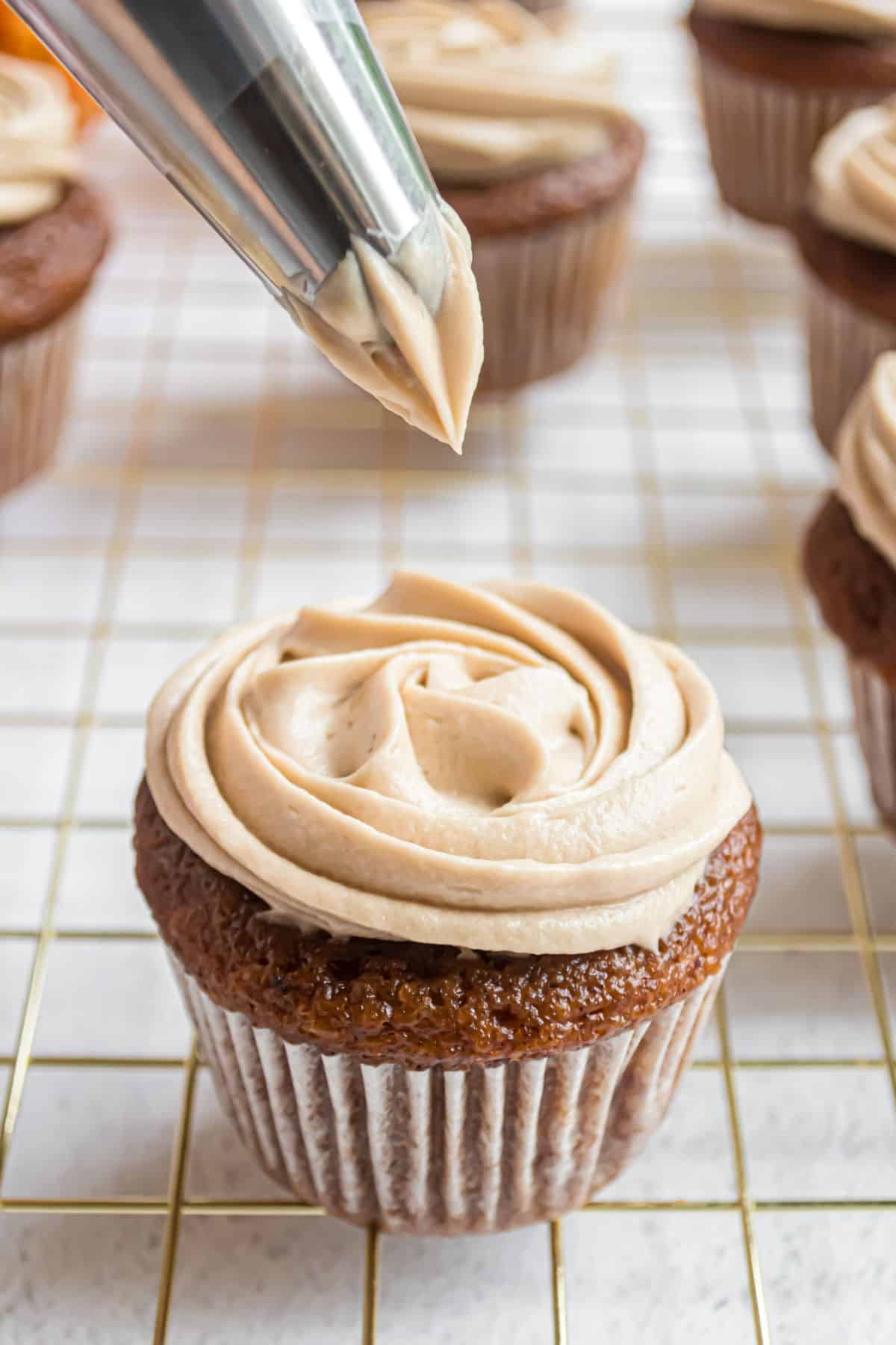 Pumpkin cupcake being frosted with maple flavored cream cheese frosting on a wire rack.