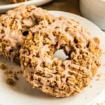 Close-up of pumpkin streusel donuts, crumb-topped and drizzled with icing, on a white plate.