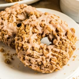 Close-up of pumpkin streusel donuts, crumb-topped and drizzled with icing, on a white plate.