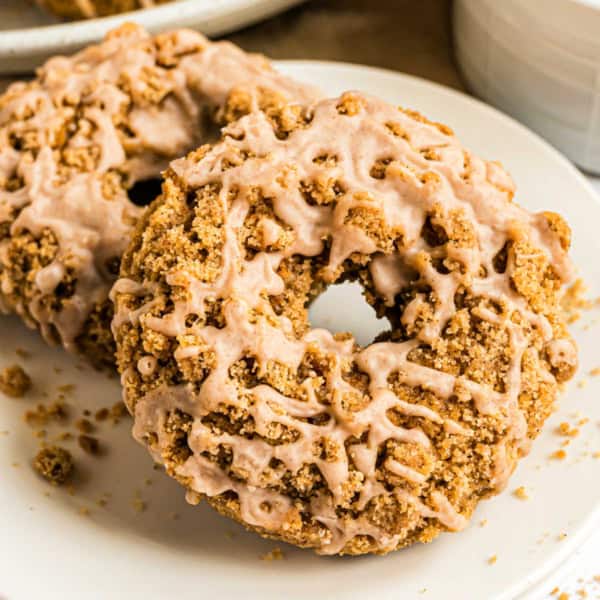 Close-up of pumpkin streusel donuts, crumb-topped and drizzled with icing, on a white plate.