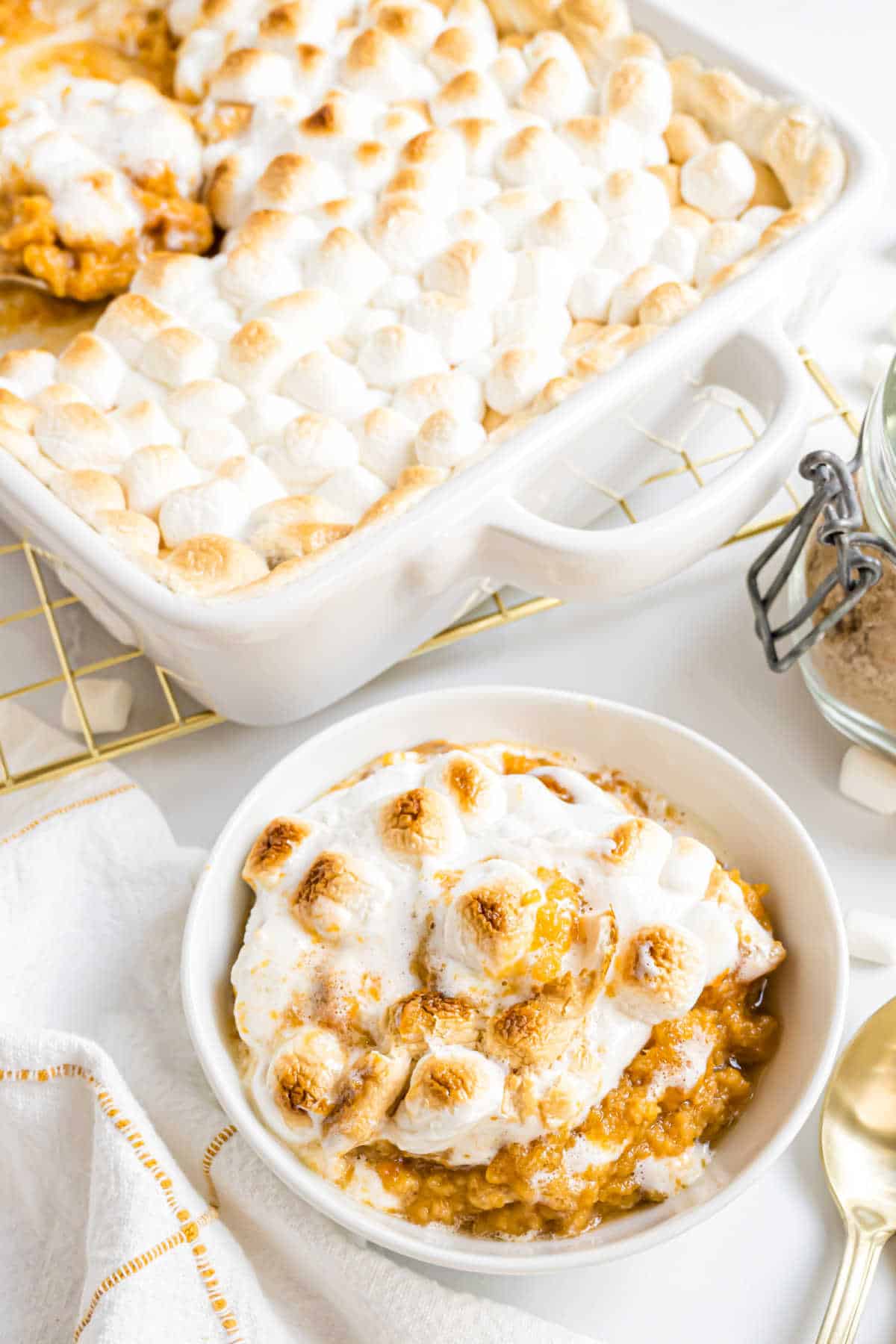 Bowl of sweet potato casserole with marshmallows, topped with perfectly toasted marshmallows, sits next to a baking dish filled with the same cozy casserole.