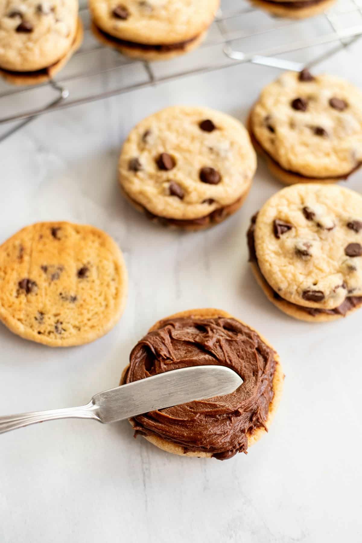 Chocolate frosting being spread on a chocolate chip cookie.