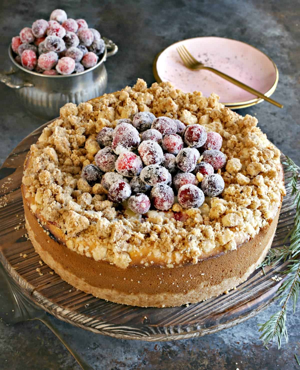 Cranberry cheesecake uncut on a wooden cake platter.