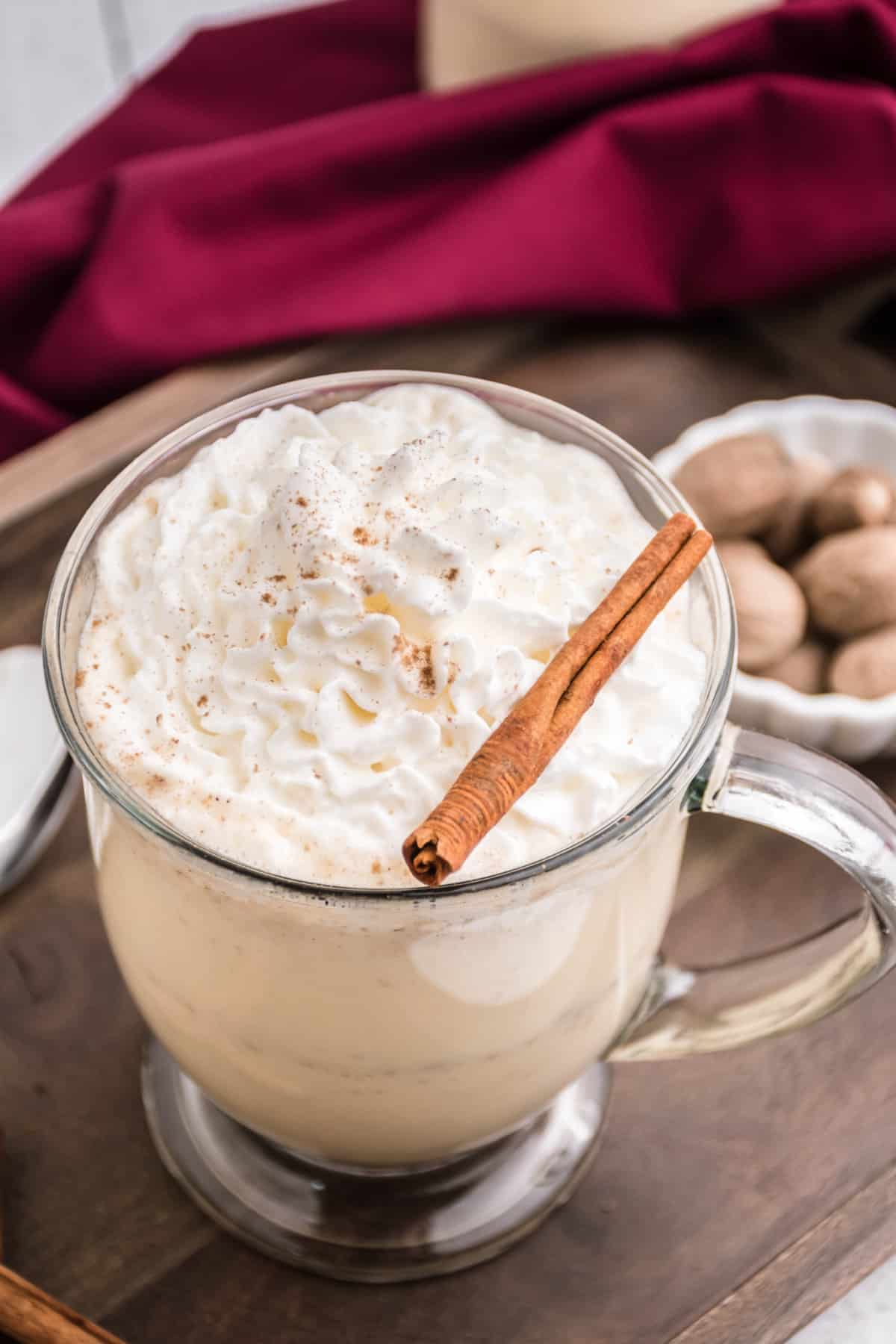 Clear glass mug with eggnog, whipped cream, and cinnamon stick.