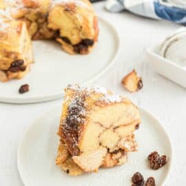 Slice of bread pudding on white plate with pressure cooker in background.