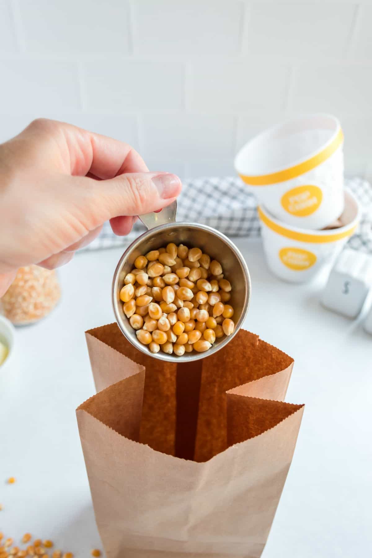 Popcorn kernels being scooped into a brown paper bag.