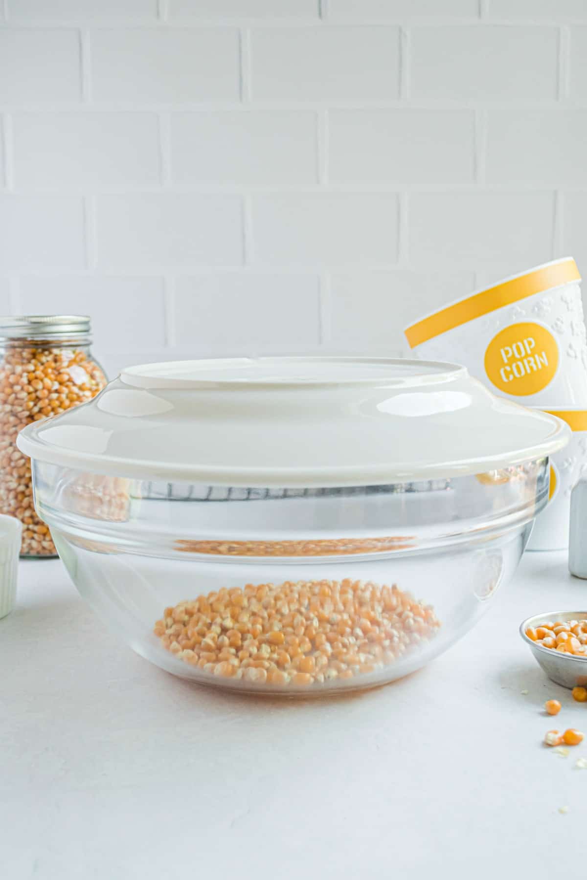 Glass bowl with white plate and popcorn kernels in bowl.