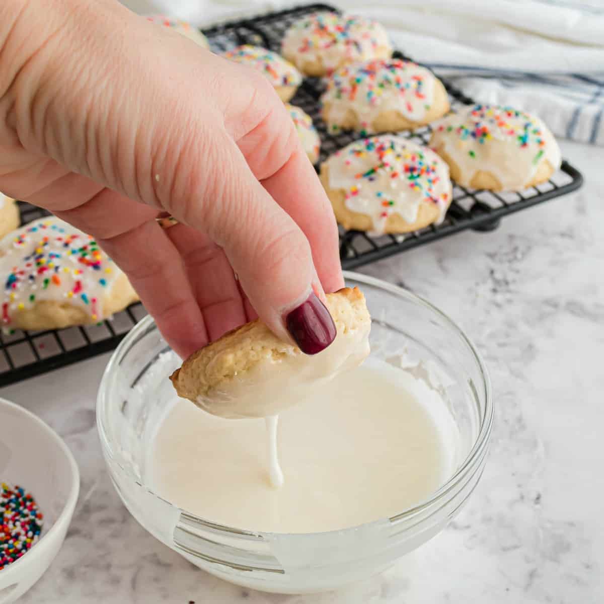 Hand holding ricotta cookie and dipping in icing.