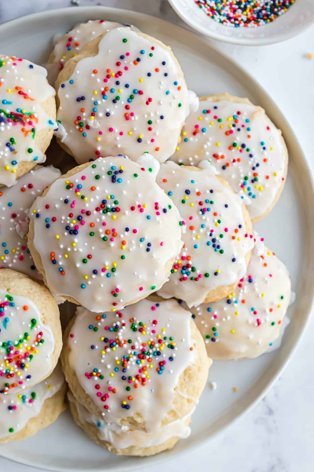 Italian ricotta cookies stacked on plate with colorful sprinkles.