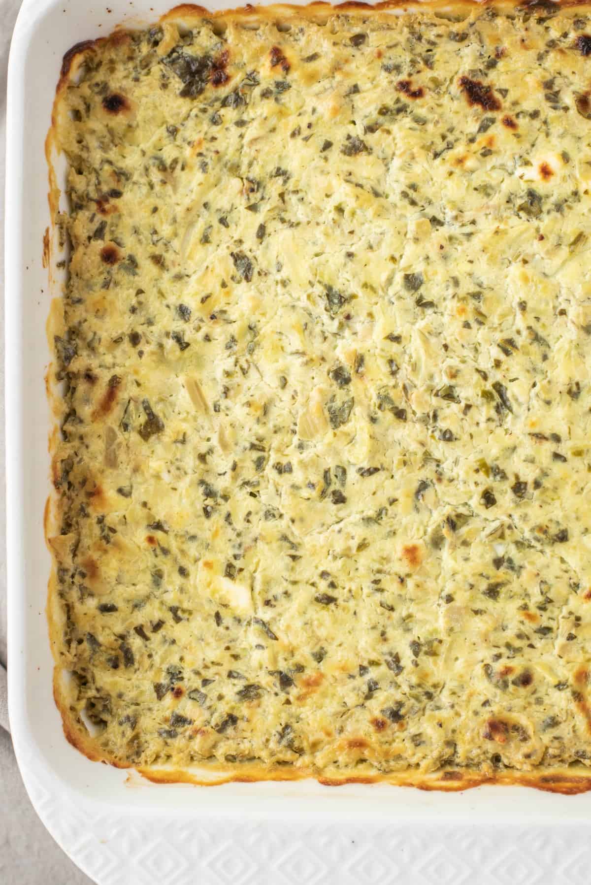 Baked spinach artichoke dip in square white baking dish.