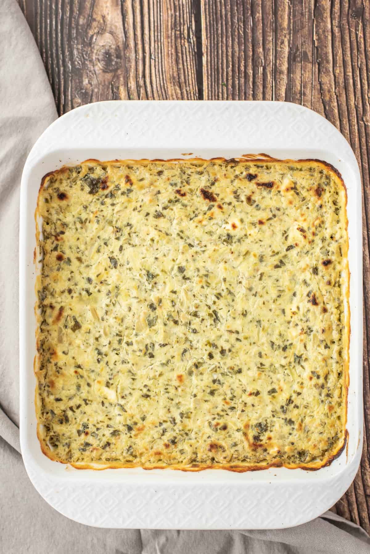 Baked spinach artichoke dip in a white baking dish.