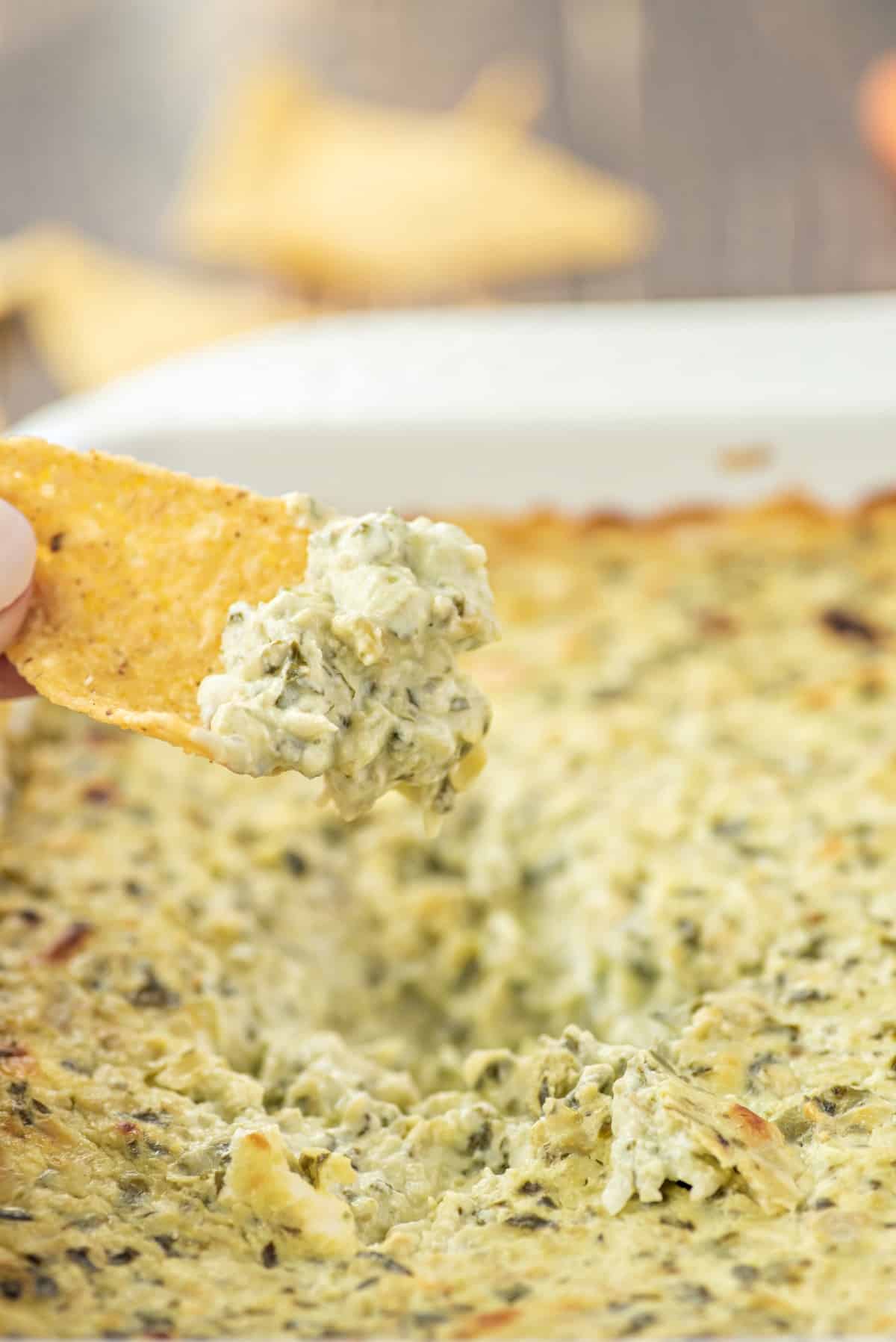 Chip scooping spinach artichoke dip out of baking dish.