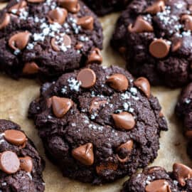 Chocolate cookies with chocolate chips and sea salt on parchment paper.