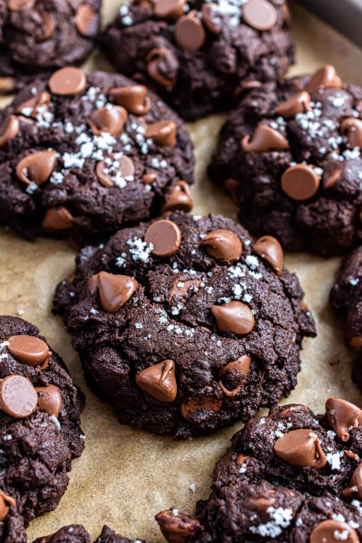 Chocolate cookies with chocolate chips and sea salt on parchment paper.