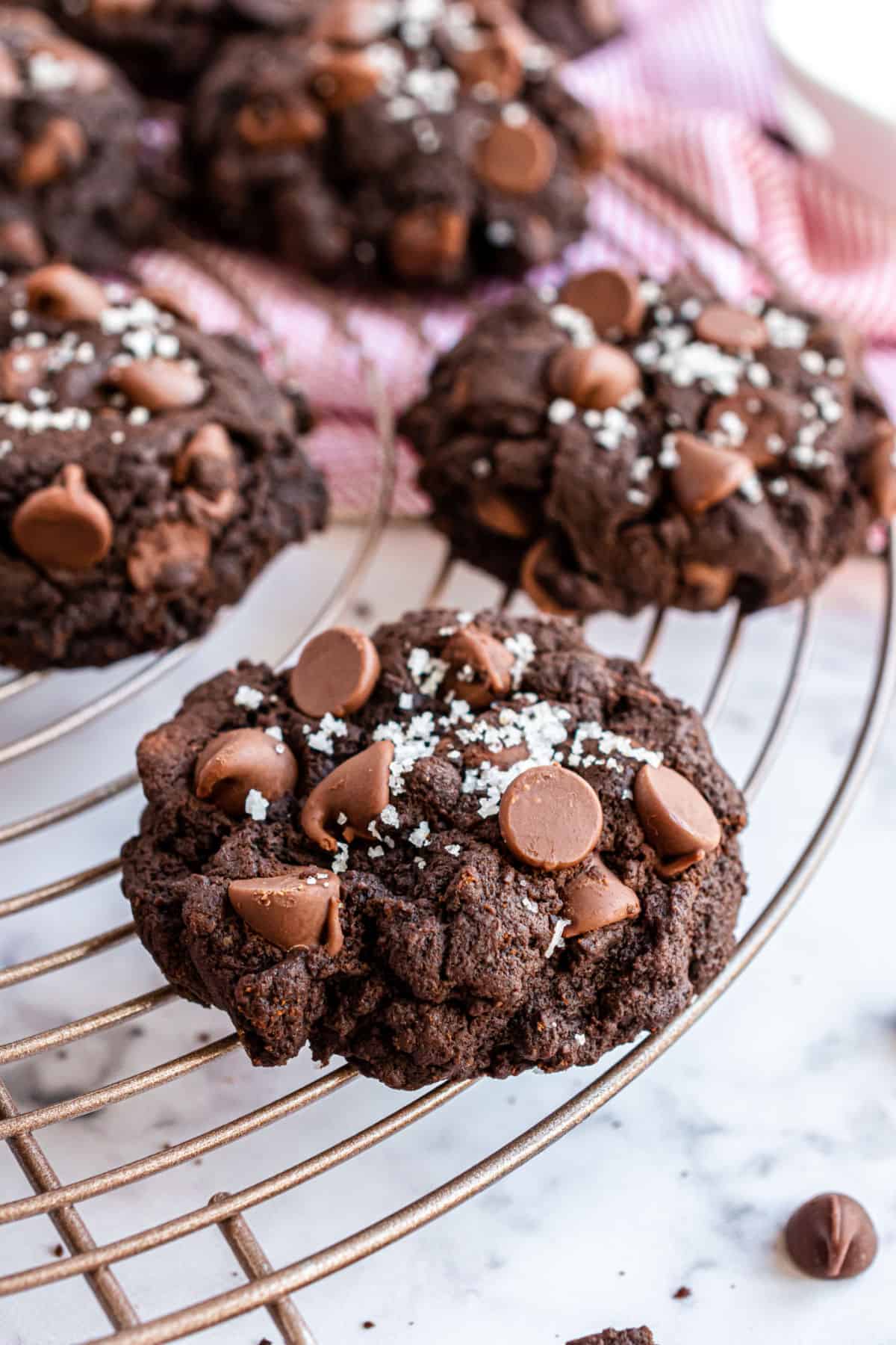 Chocolate cookie with chocolate chips and flake sea salt on a wire rack.