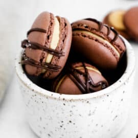 Chocolate macarons with peanut butter filling in a white marble cup.