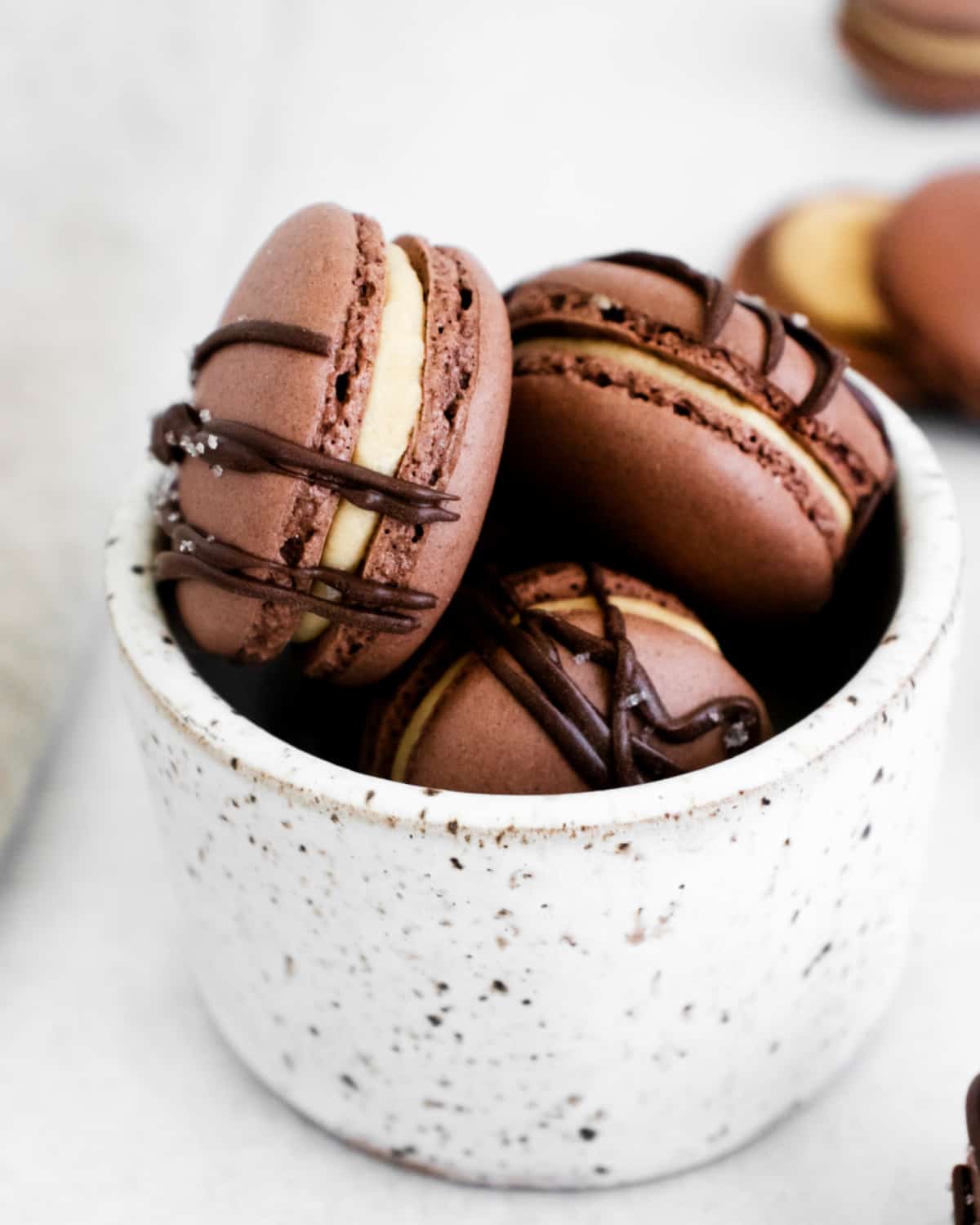 Chocolate macarons with peanut butter filling in a white marble cup.