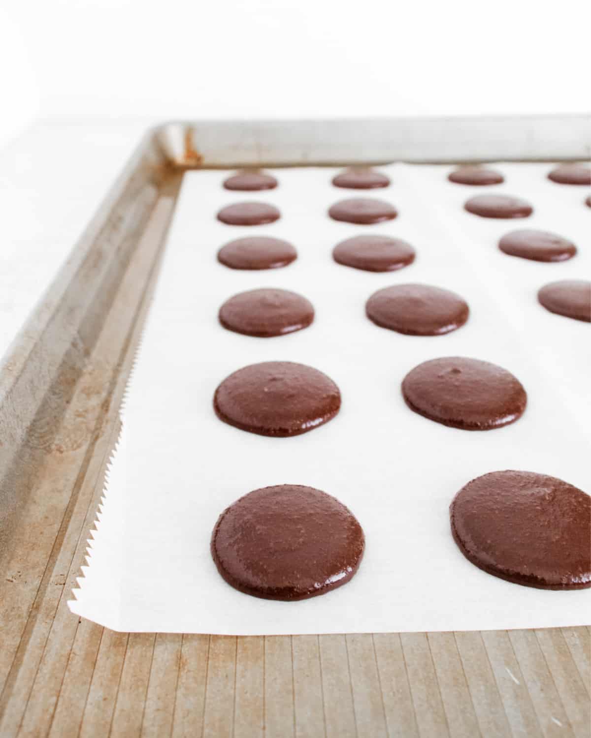 Piped macaron batter on parchment paper lined cookie sheet.
