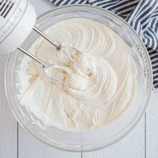 Cream cheese frosting in glass bowl with hand mixer.