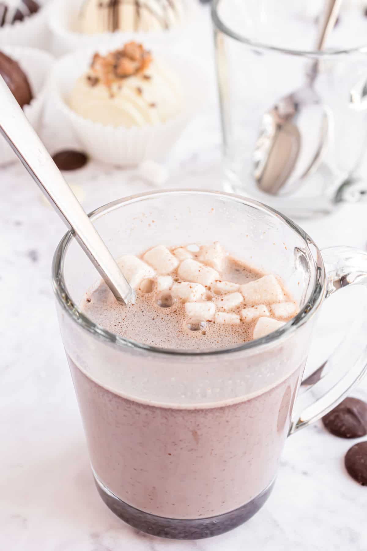 Hot cocoa bomb with marshmallows dissolved in clear mug of warm milk.