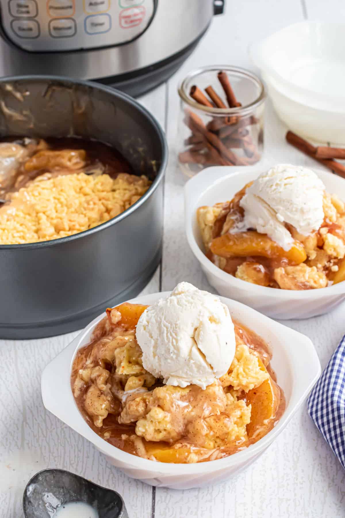 Peach cobbler made in the pressure cooker and served in a white bowl with vanilla ice cream.