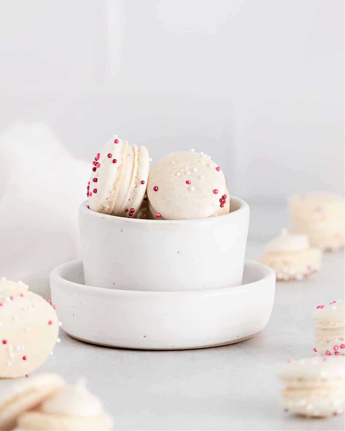 Vanilla macarons in a white bowl with pink sprinkles.