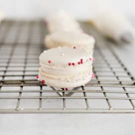 Vanilla bean macarons with pink sprinkles on a wire rack.