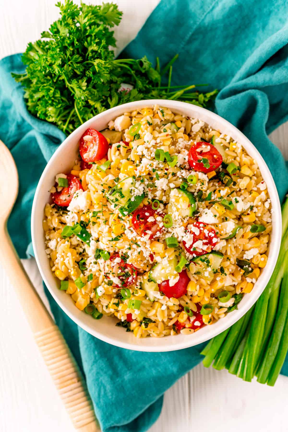 Orzo salad served in white bowl with wooden spoon and fresh parsley.