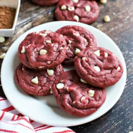 Red velvet cookies with white chocolate chips stacked on a white plate.