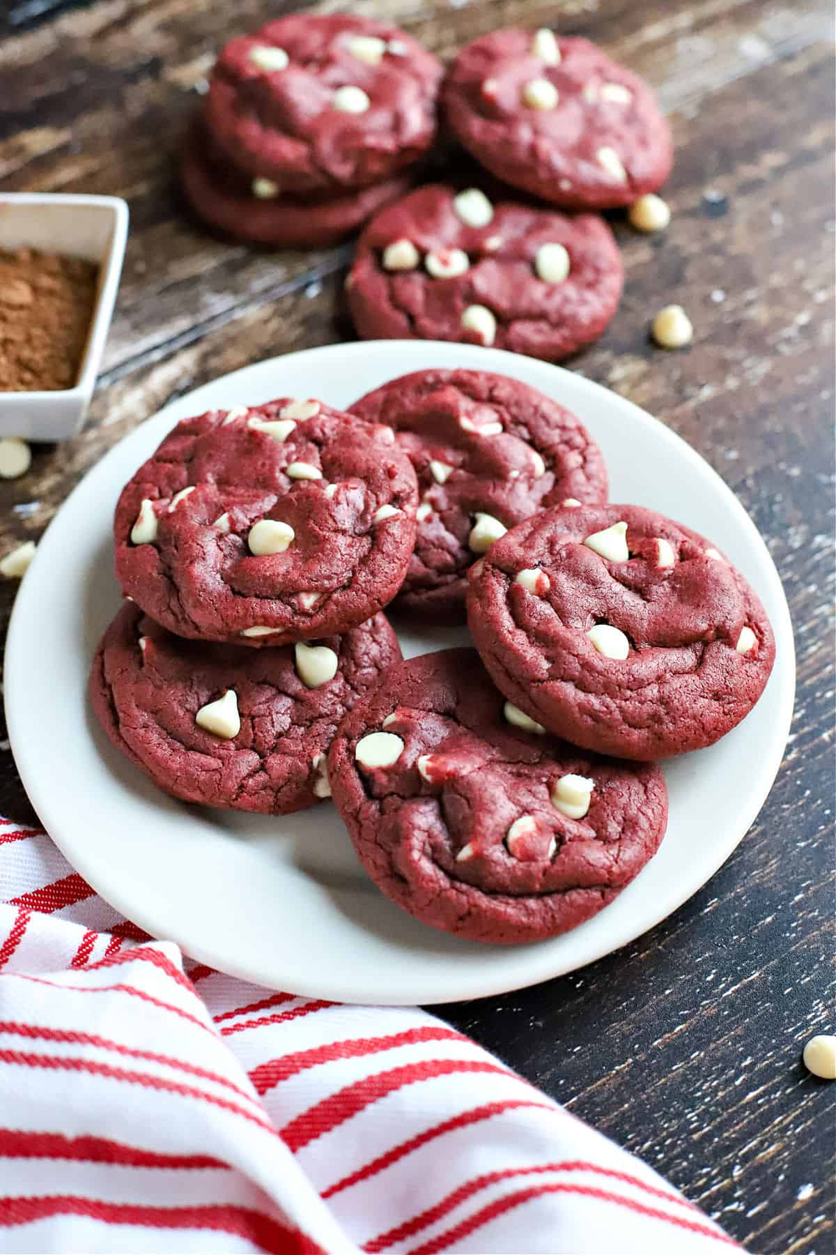 Red velvet cookies with white chocolate chips stacked on a white plate.