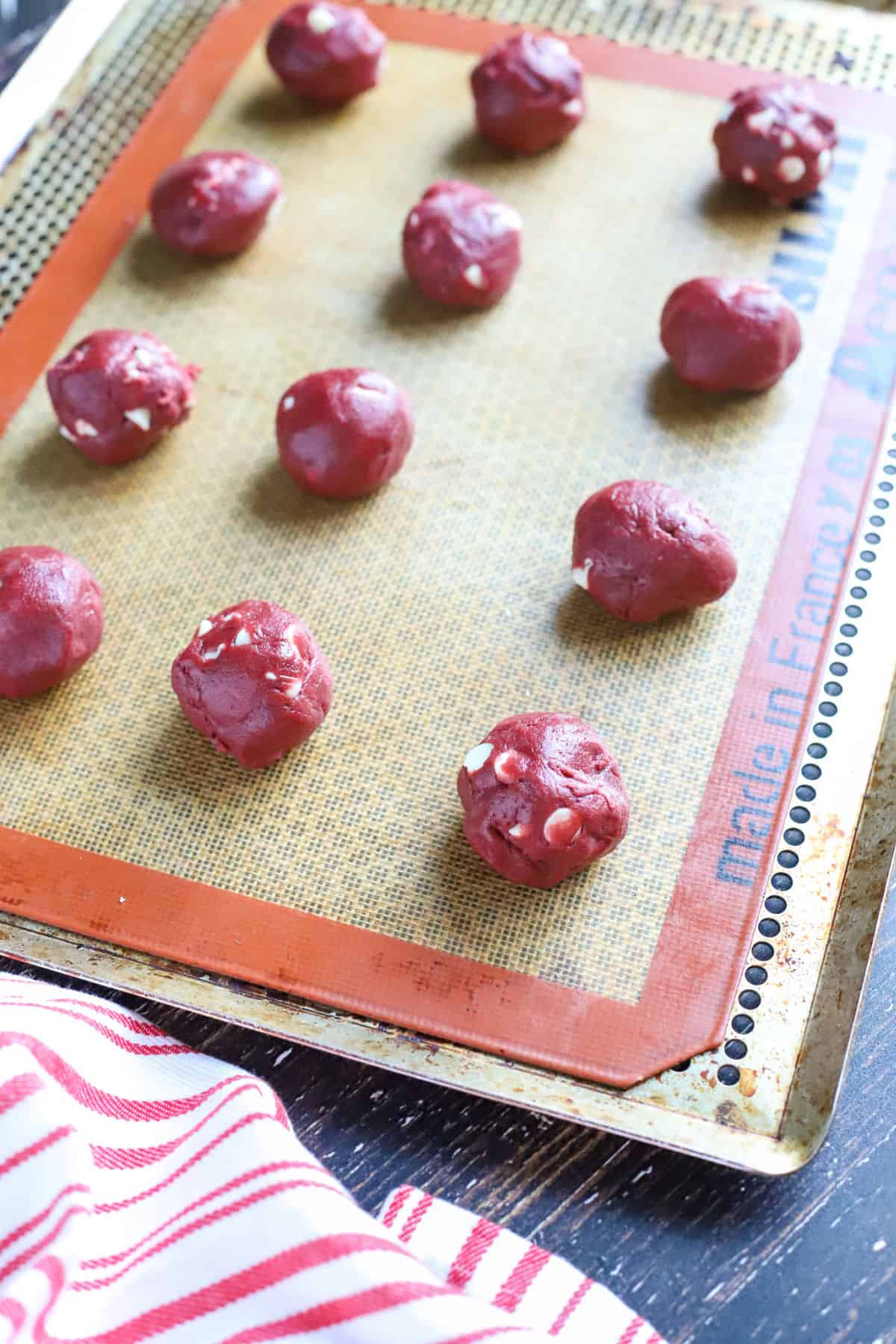 Red velvet cookie dough rolled into balls on a cookie sheet.