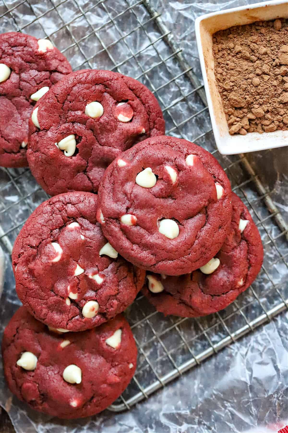 Red velvet cookies with white chocolate chips on a wire cooling rack.