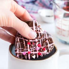 Valentine's hot cocoa bomb being placed in a mug for hot chocolate.